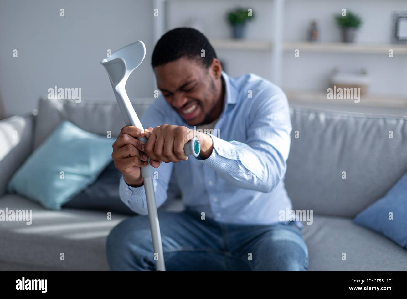 Giovane uomo nero che soffre di dolore acuto, appoggiato su crutch a casa, fuoco selettivo Foto Stock