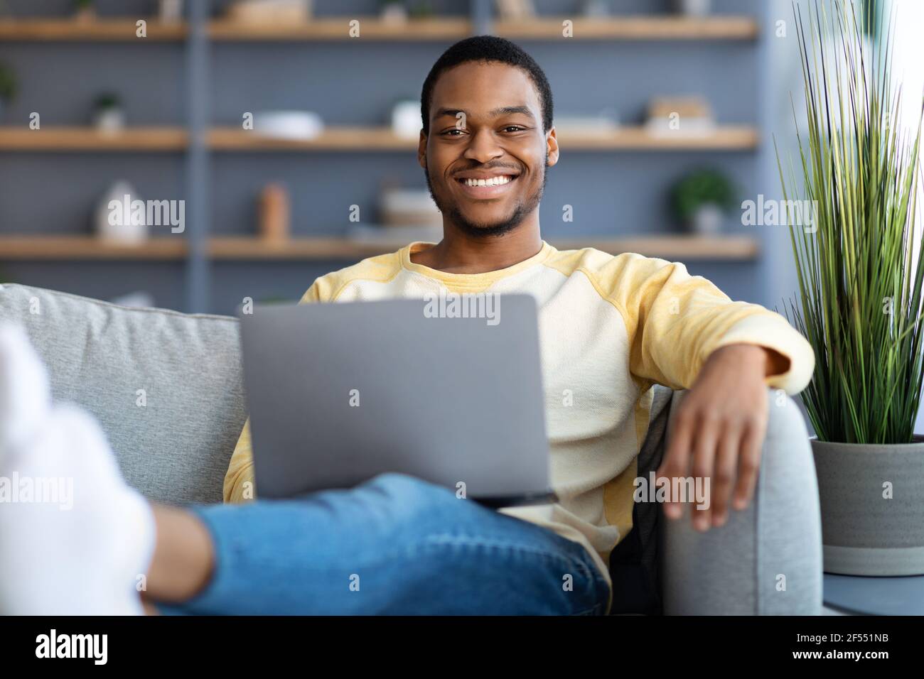 Uomo nero positivo che si agghiacciano sul divano, usando il computer portatile Foto Stock