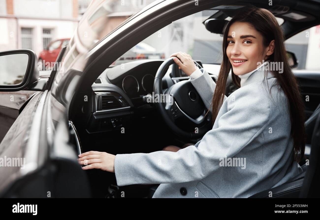 Donna d'affari riuscita uscire dall'auto e sorridere. Dirigente femminile che si trova a bordo di un veicolo per guidare al lavoro Foto Stock
