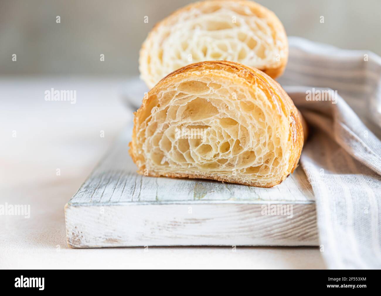 Tagliare a metà croissant con consistenza interna e strati sottili e croccanti su tavola di legno, fondo di cemento chiaro. Deliziosa pasticceria francese. Messa a fuoco selettiva. Foto Stock