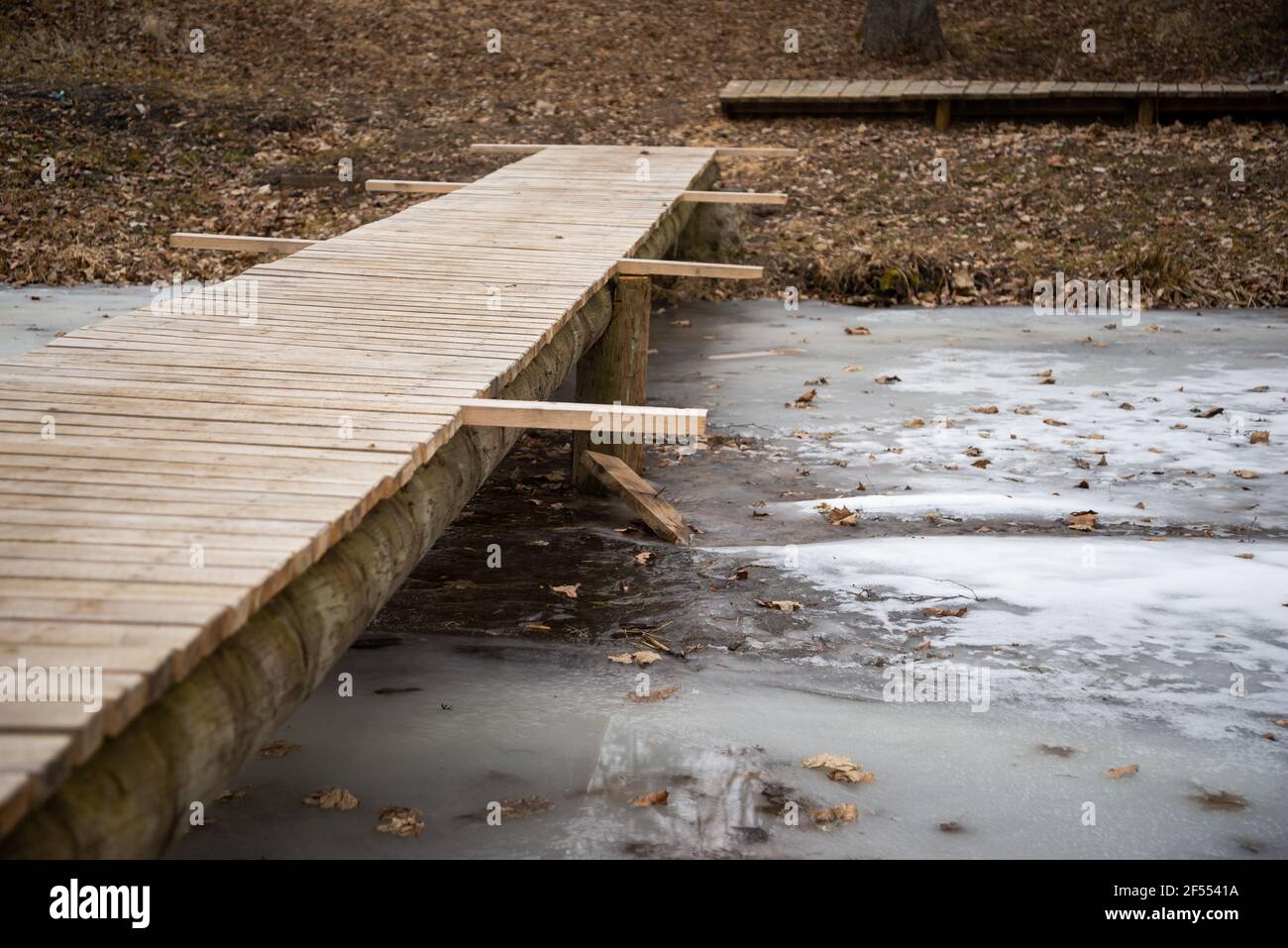 ponte pedonale in legno fatto di tavole di legno su un fiume ghiacciato in primavera. Il ponte è ancora in costruzione senza installato prototiv Foto Stock
