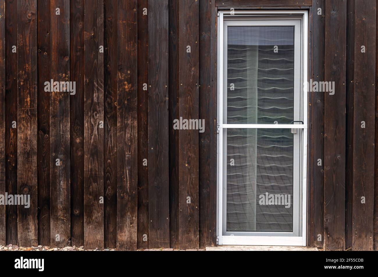 Vecchia facciata in legno di un edificio residenziale con una nuova porta con schermo a mosca integrata nella porta del patio Foto Stock