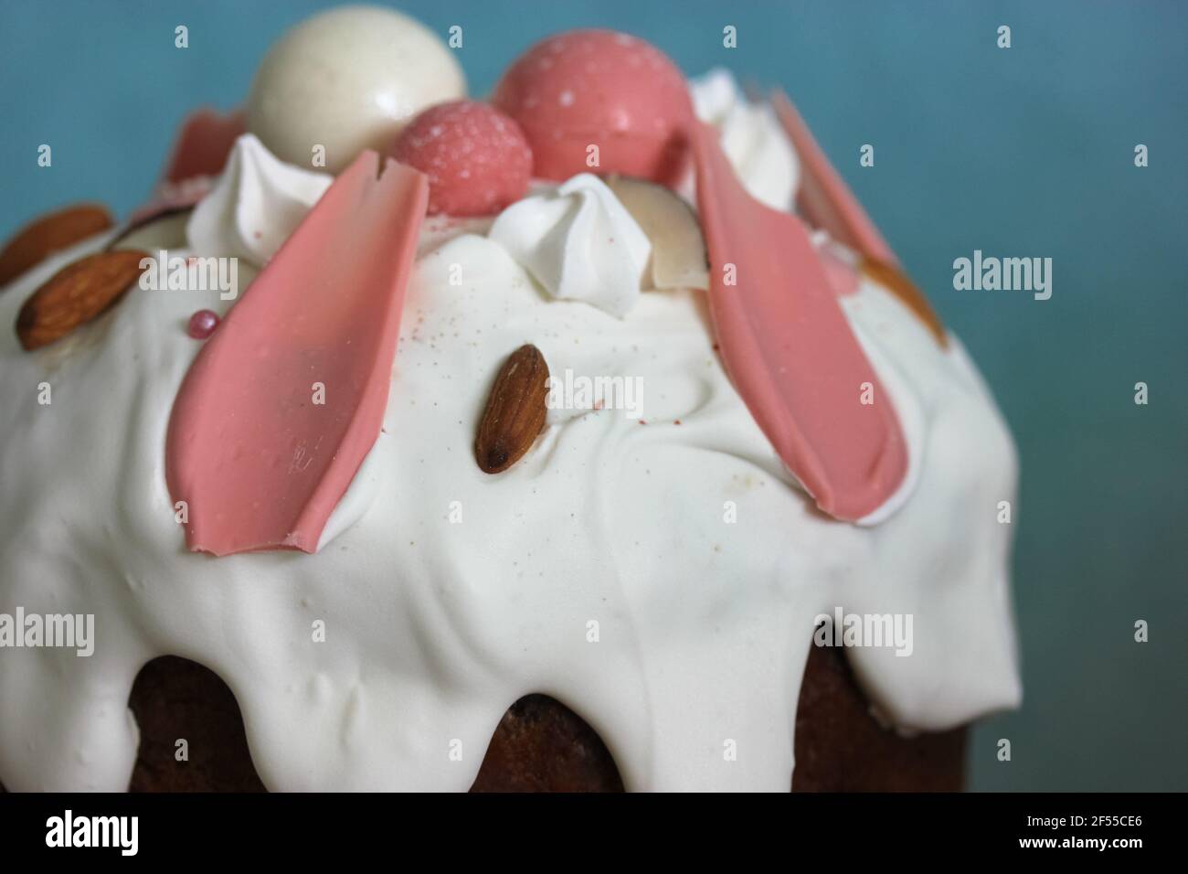 Torta di Pasqua decorata con glassa bianca, meringa, palline di cioccolato decorative rosa, noci. Pane pasquale fatto in casa vista dall'alto su sfondo blu. Una ricetta f Foto Stock