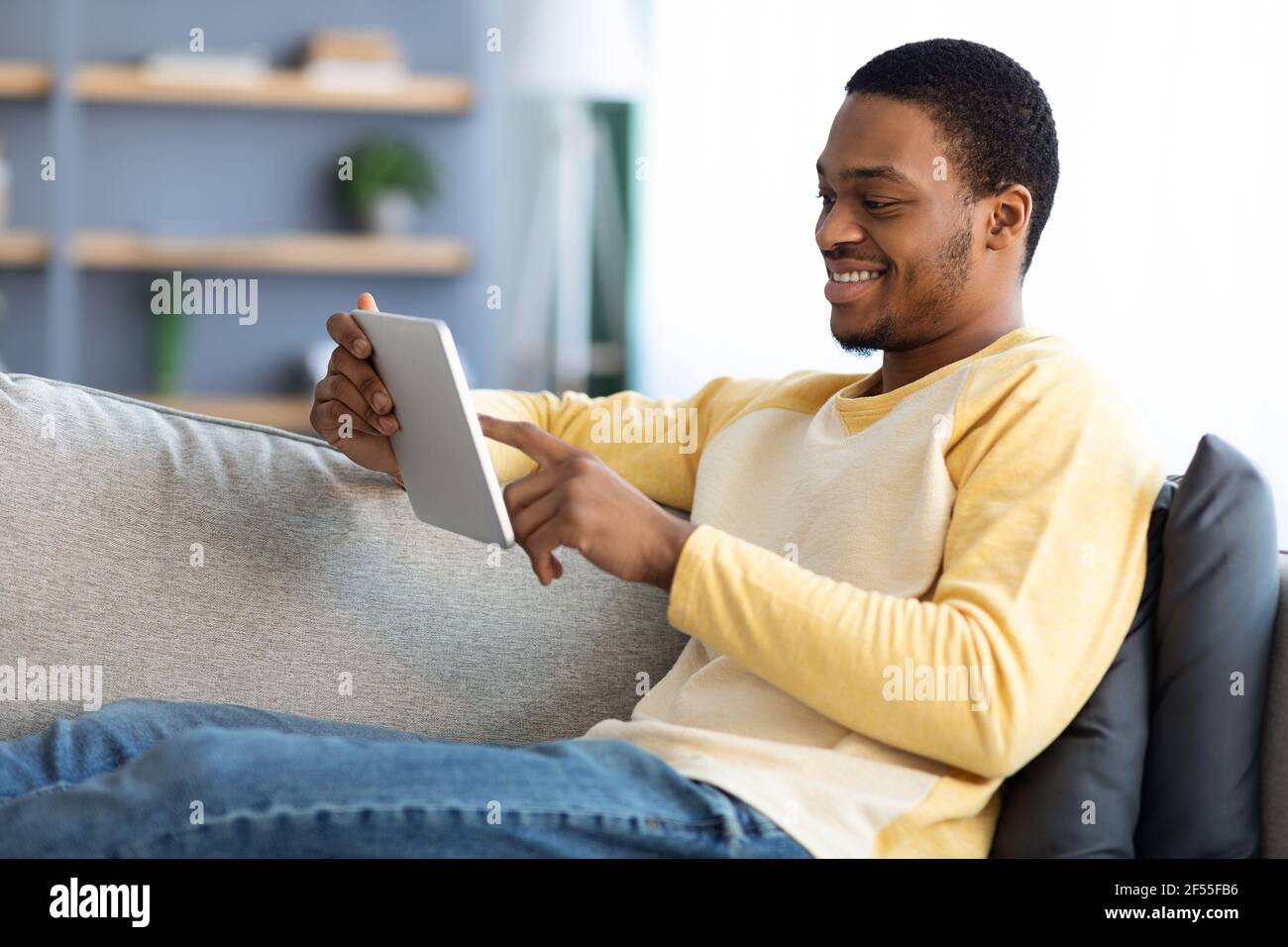 Felice americano aficano che riposa sul divano, usando un tablet digitale Foto Stock
