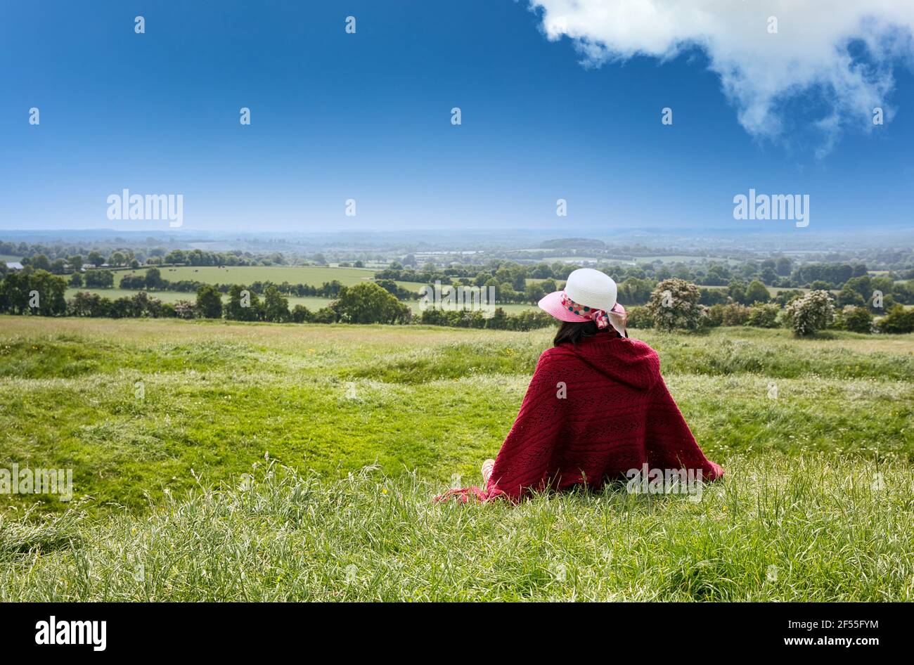 Donna seduta in campi erbosi fattoria mentre si guarda orizzonte Foto Stock