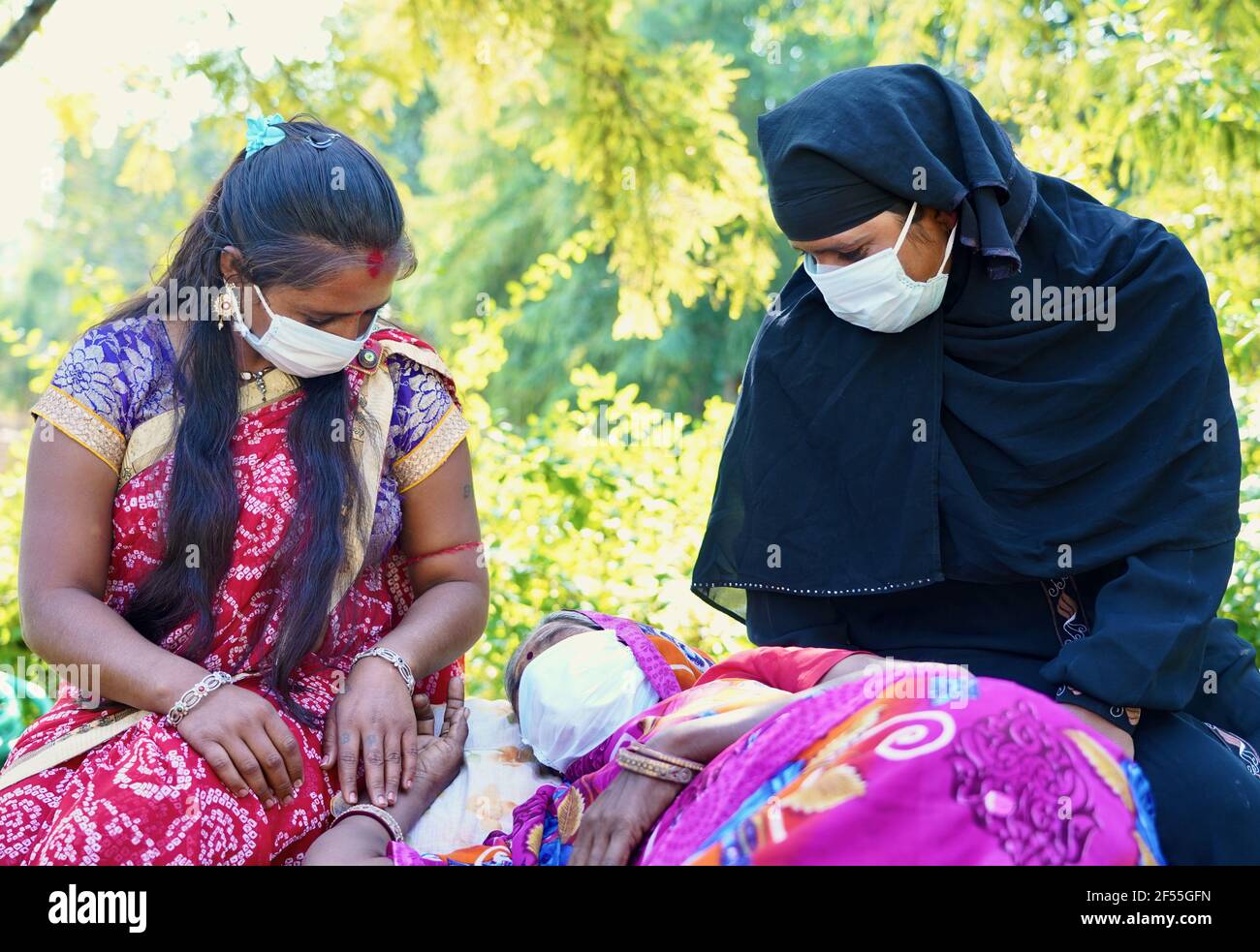 Closeup di tre donne indiane con una di loro sdraiata, tutte con maschera facciale durante la luce del giorno Foto Stock