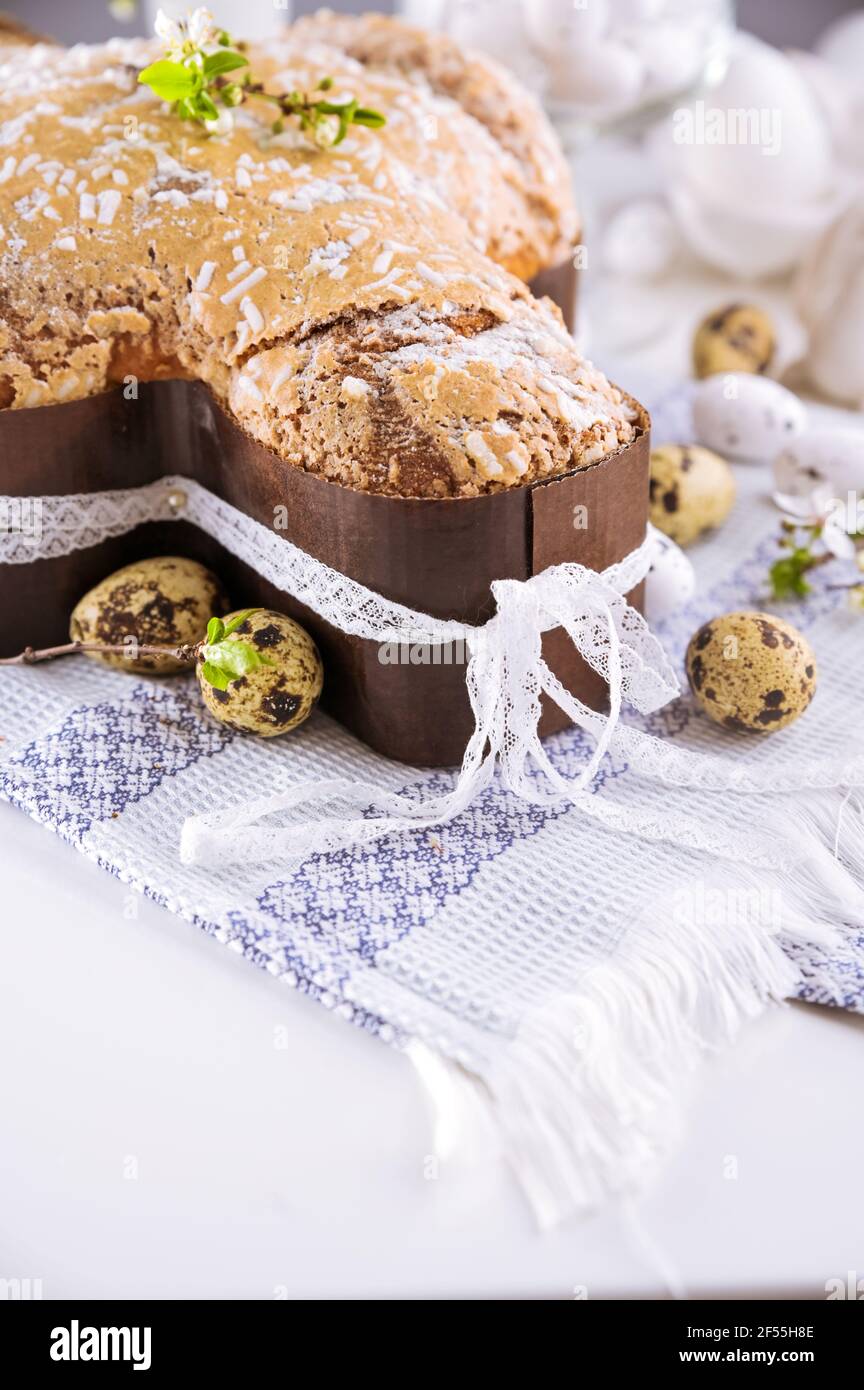 Dessert tradizionali italiani per Pasqua - colomba di Pasqua. Dolci natalizi con mandorle e glassa di zucchero su sfondo chiaro e rami fioriti, decorazioni pasquali e uova. Verticale. Primo piano Foto Stock