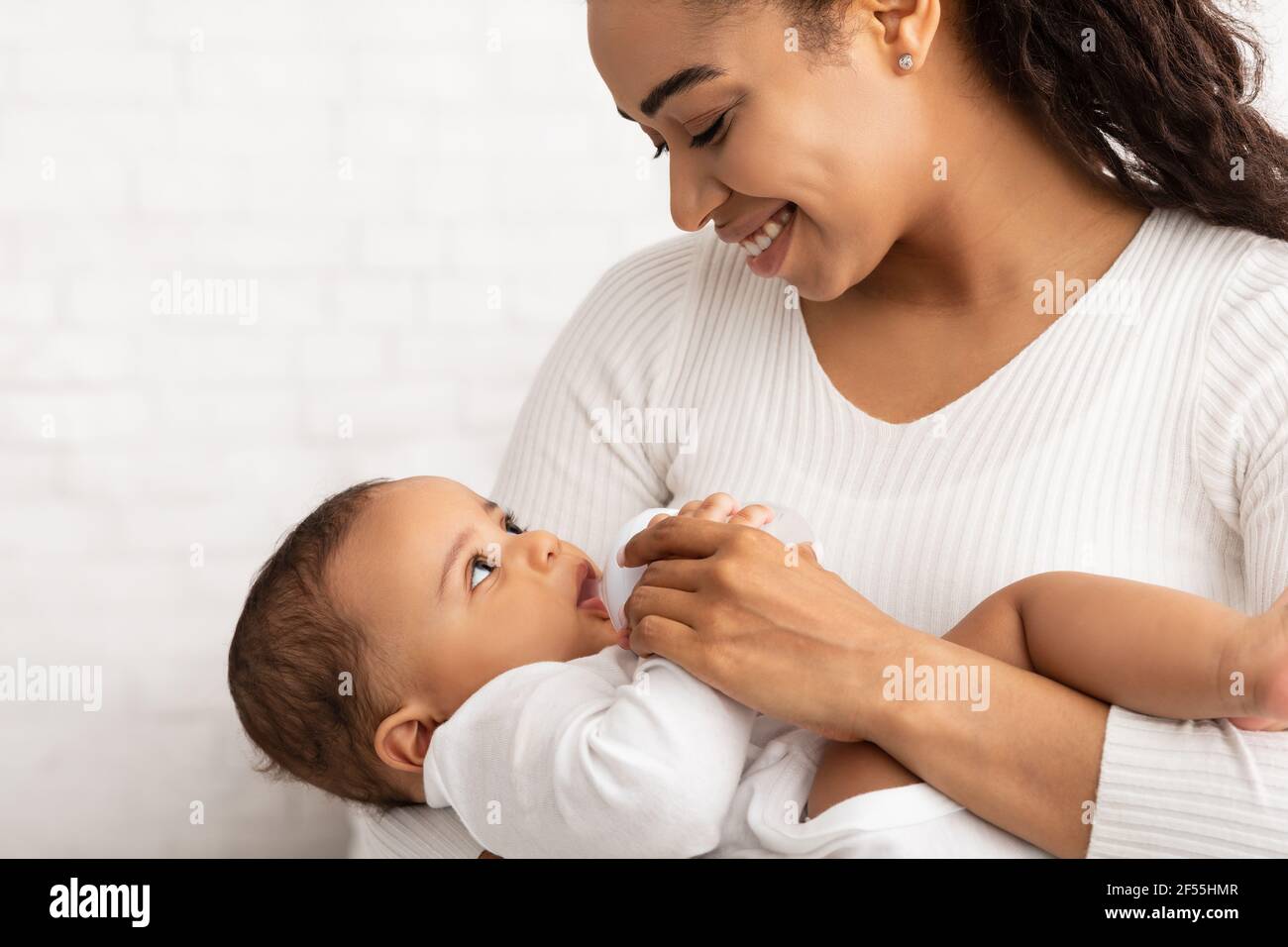 Happy Black Madre che alimenta neonato biberon che dà, sfondo bianco Foto Stock