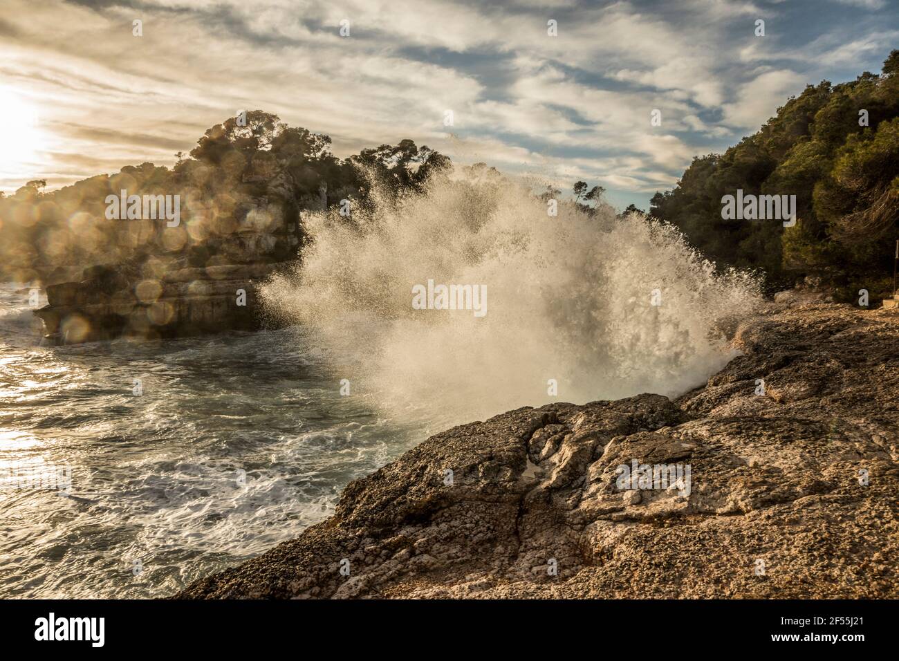 Spagna, Maiorca, le onde del mare si infrangono contro le rocce sulla spiaggia di Cala des Moro al tramonto Foto Stock