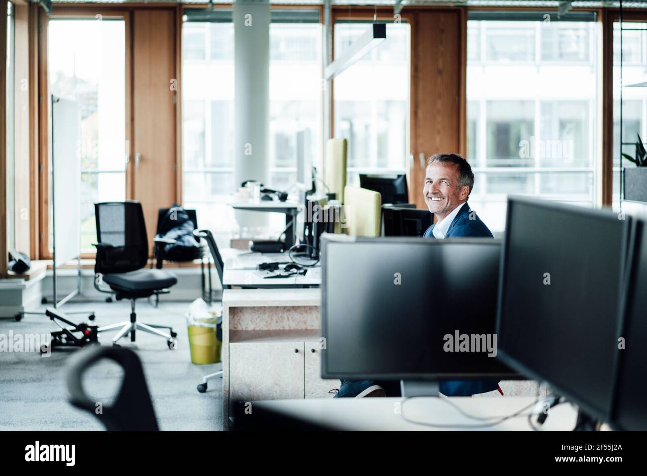 Uomo d'affari sorridente seduto tra i computer in ufficio Foto Stock