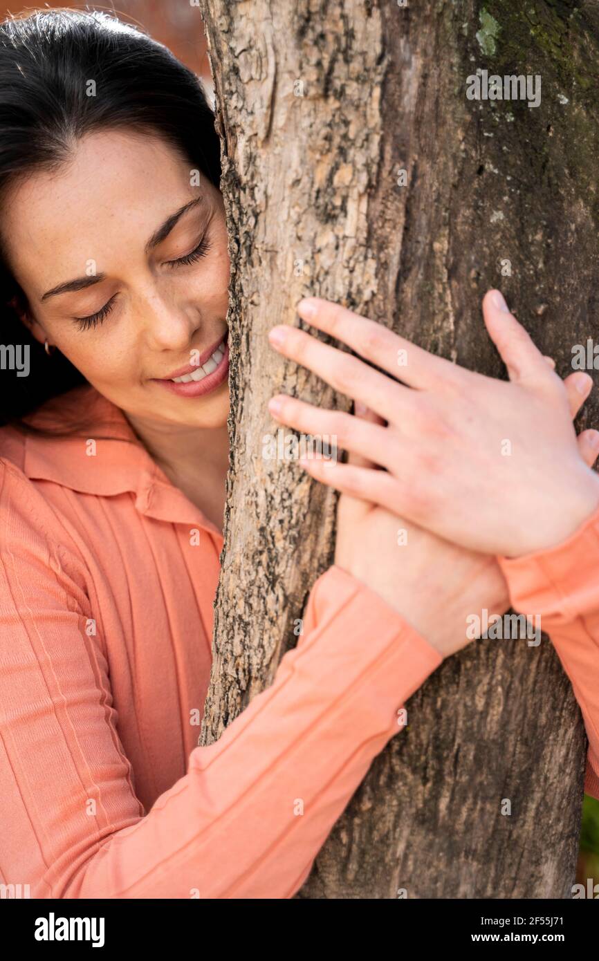 Donna affettuosa che abbraccia il tronco dell'albero in giardino Foto Stock
