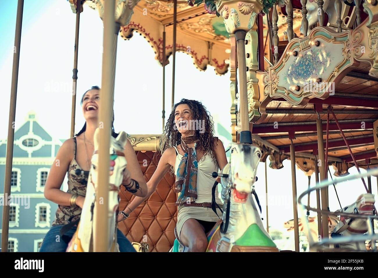 Felici le giovani donne che ridono mentre cavalcano i cavalli della giostra nel divertimento parcheggio Foto Stock