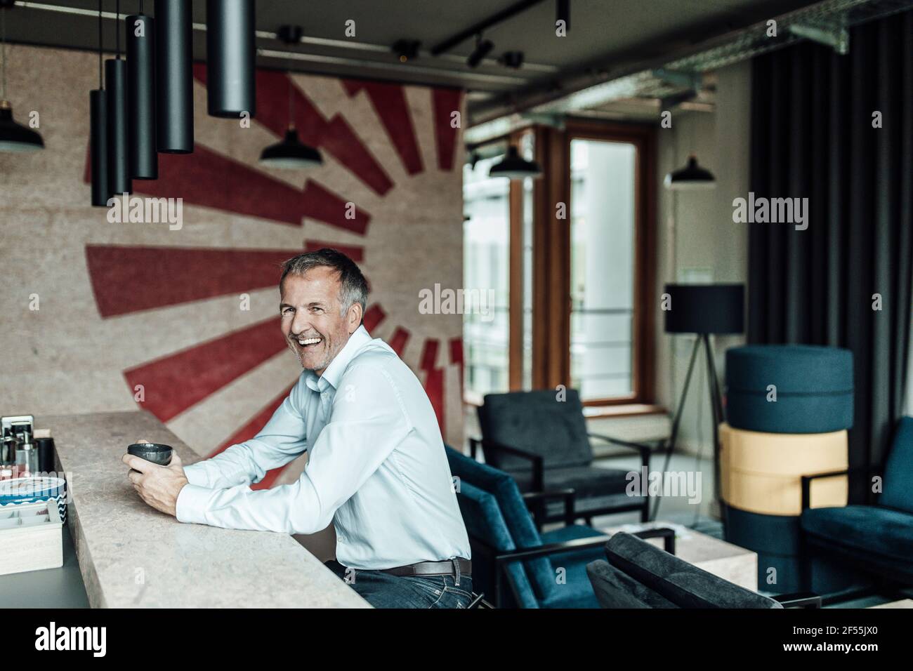Uomo d'affari ridente con la tazza del tè che guarda via mentre sedendo a. tavolo in caffetteria Foto Stock