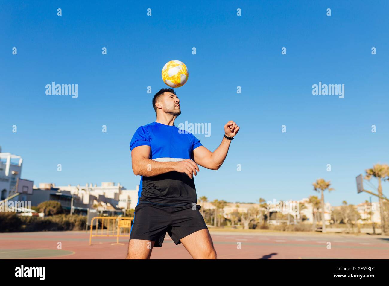 Uomo maturo che gioca con la palla di calcio sul campo sportivo durante giorno di sole Foto Stock