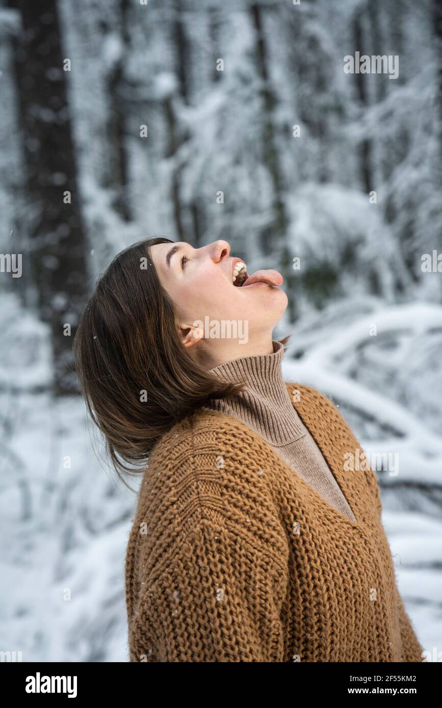 Donna giocosa che si stacca la lingua mentre si trova in piedi nella foresta Foto Stock