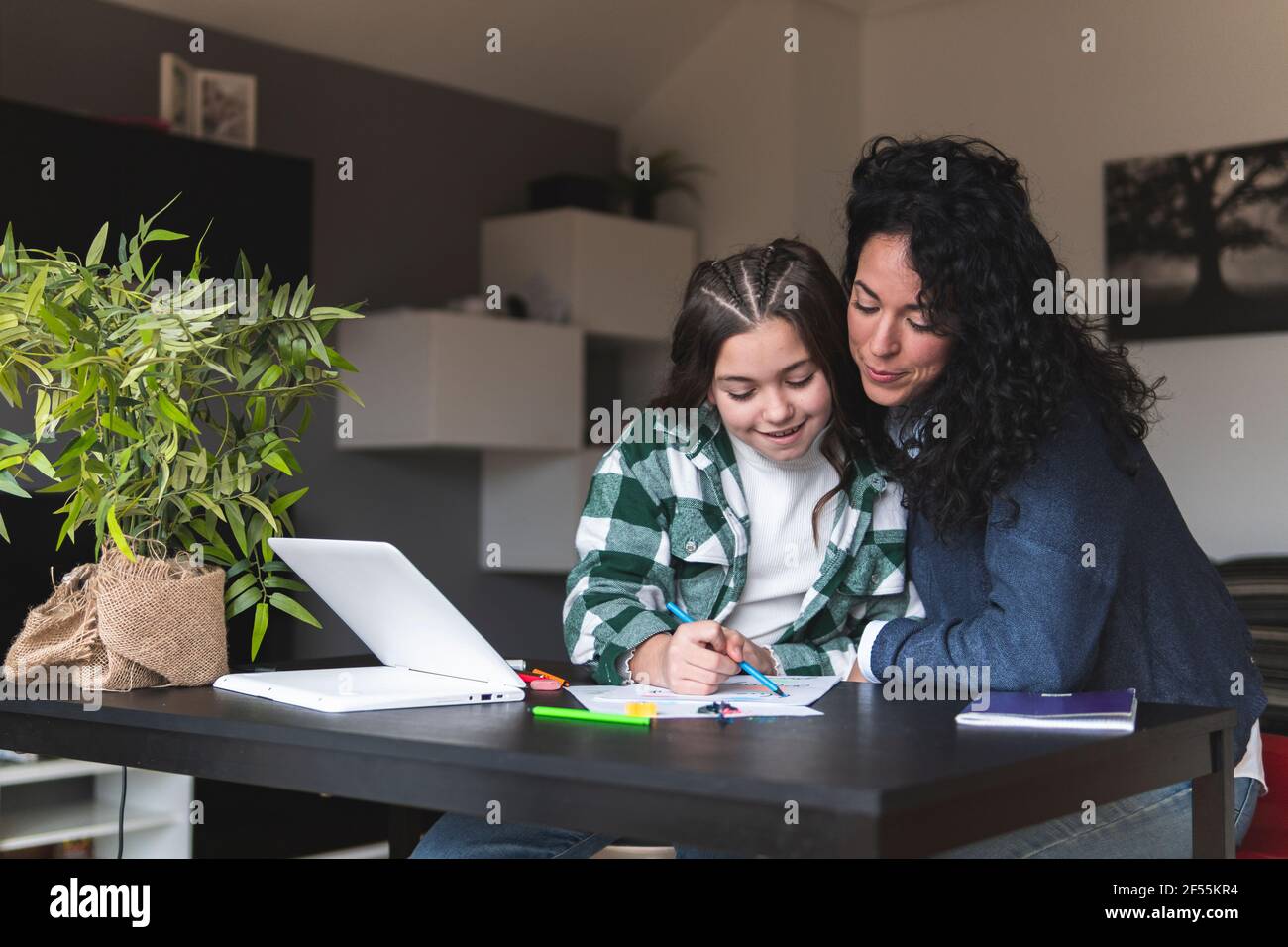 Madre che assiste la figlia mentre studia al tavolo in soggiorno Foto Stock