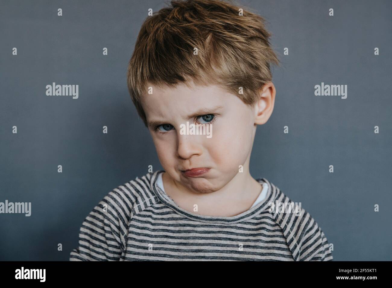Ragazzo innocente che fa faccia su sfondo grigio Foto Stock