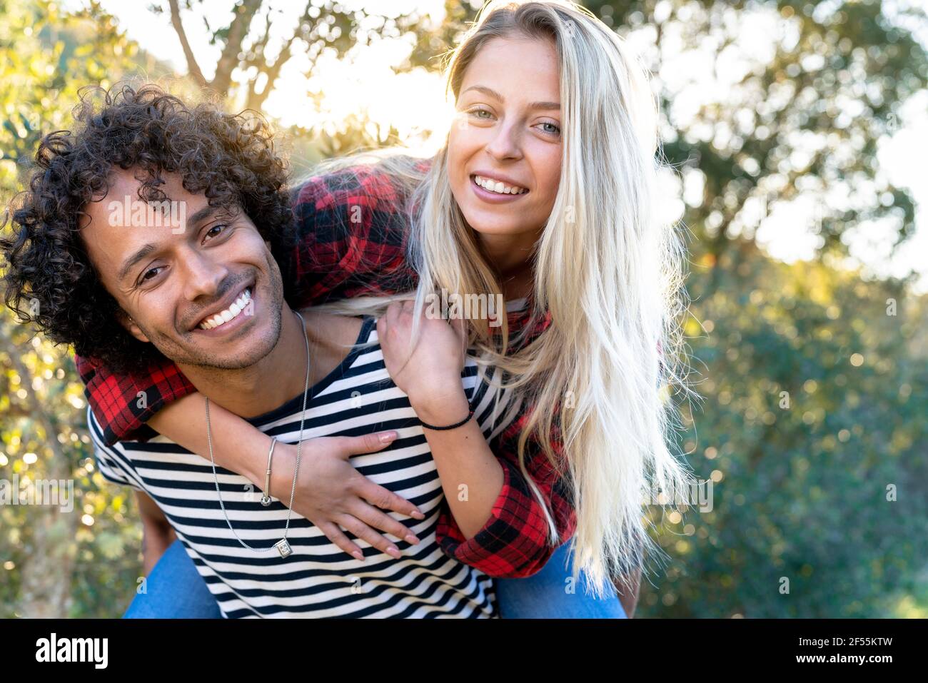 Giocosa donna piggybacking su uomo sorridente mentre in piedi davanti o cortile posteriore Foto Stock