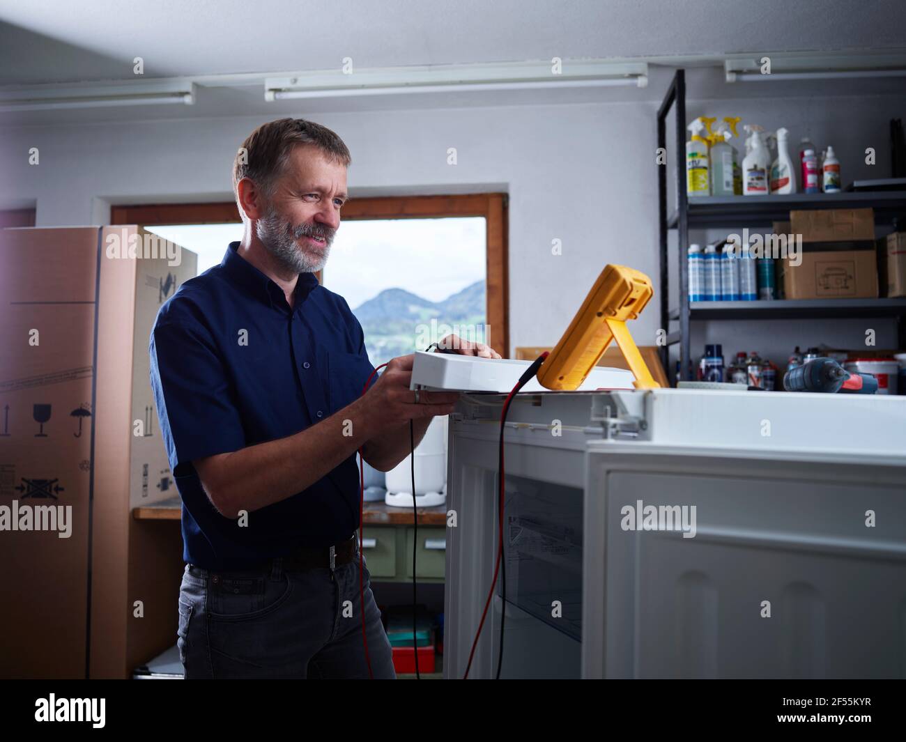 Elettricista maschio che misura l'alimentazione elettrica attraverso il multimetro presso l'officina elettrica Foto Stock