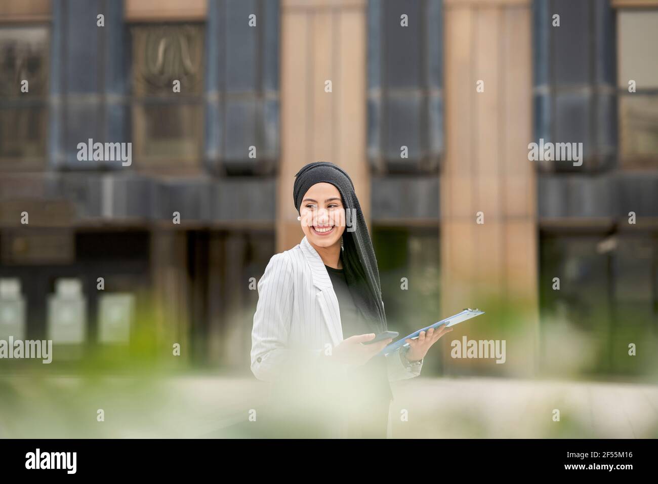 Donna d'affari araba sorridente che guarda lontano mentre si alza in piedi all'aperto Foto Stock