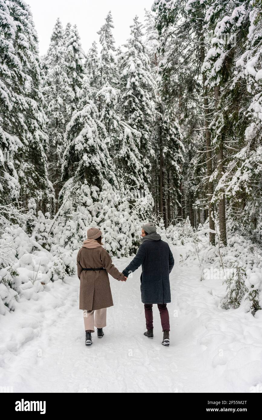 Coppia che tiene le mani mentre si cammina su un percorso forestale innevato Foto Stock