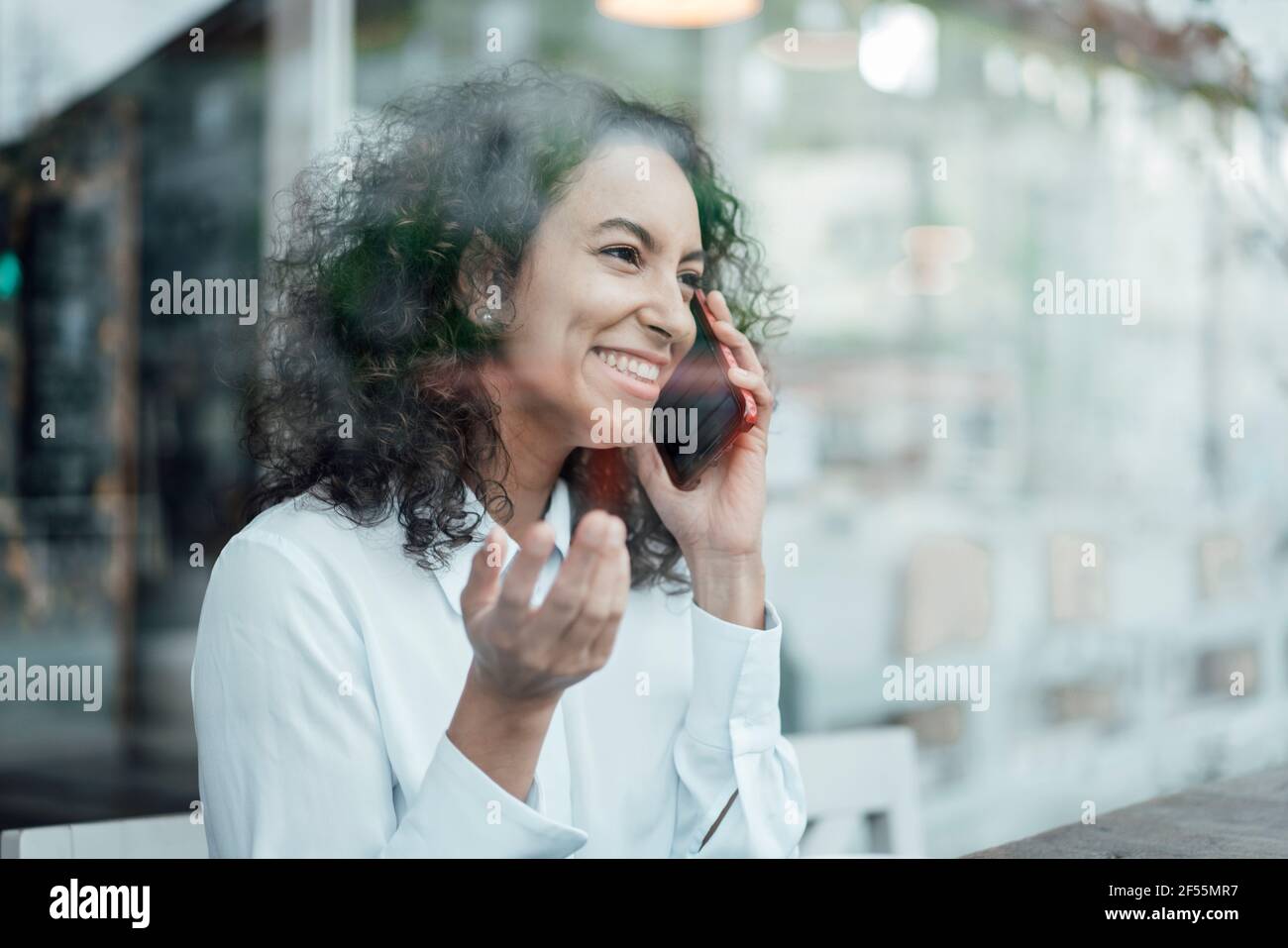 Giovane donna d'affari sorridente mentre parla sul telefono cellulare seduto a. caffè Foto Stock