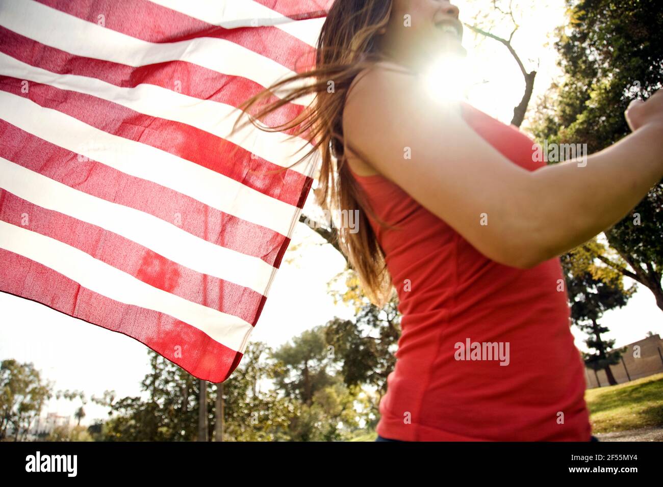Giovane donna che corre nel parco mentre tiene la bandiera americana durante giorno di sole Foto Stock