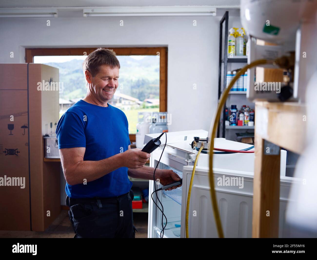 Sorridente elettricista maschio che tiene l'attrezzatura durante il controllo della temperatura in officina Foto Stock
