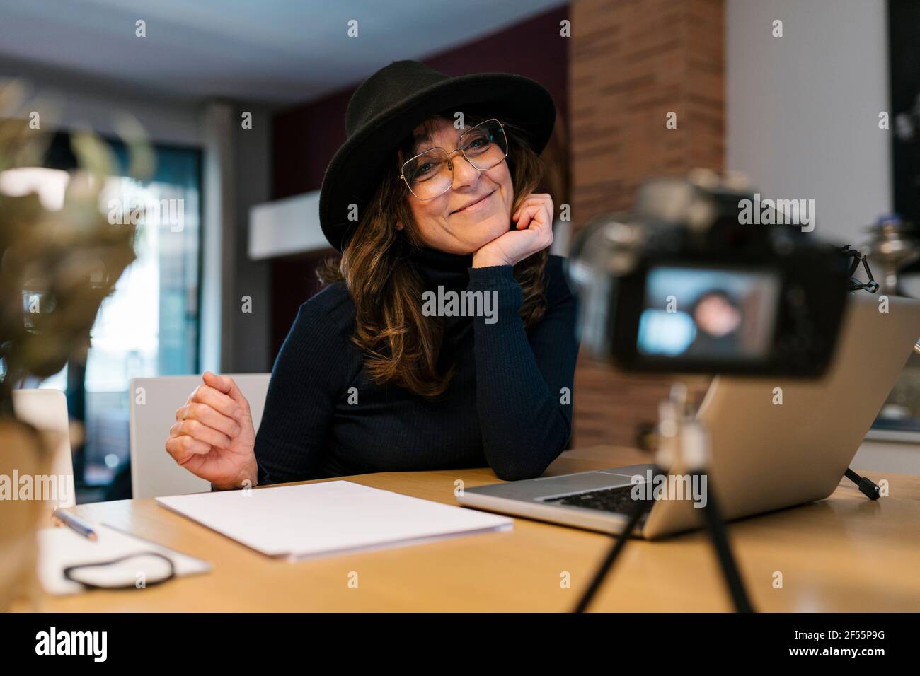 Donna che indossa un cappello sorridente mentre filma con la fotocamera a casa Foto Stock
