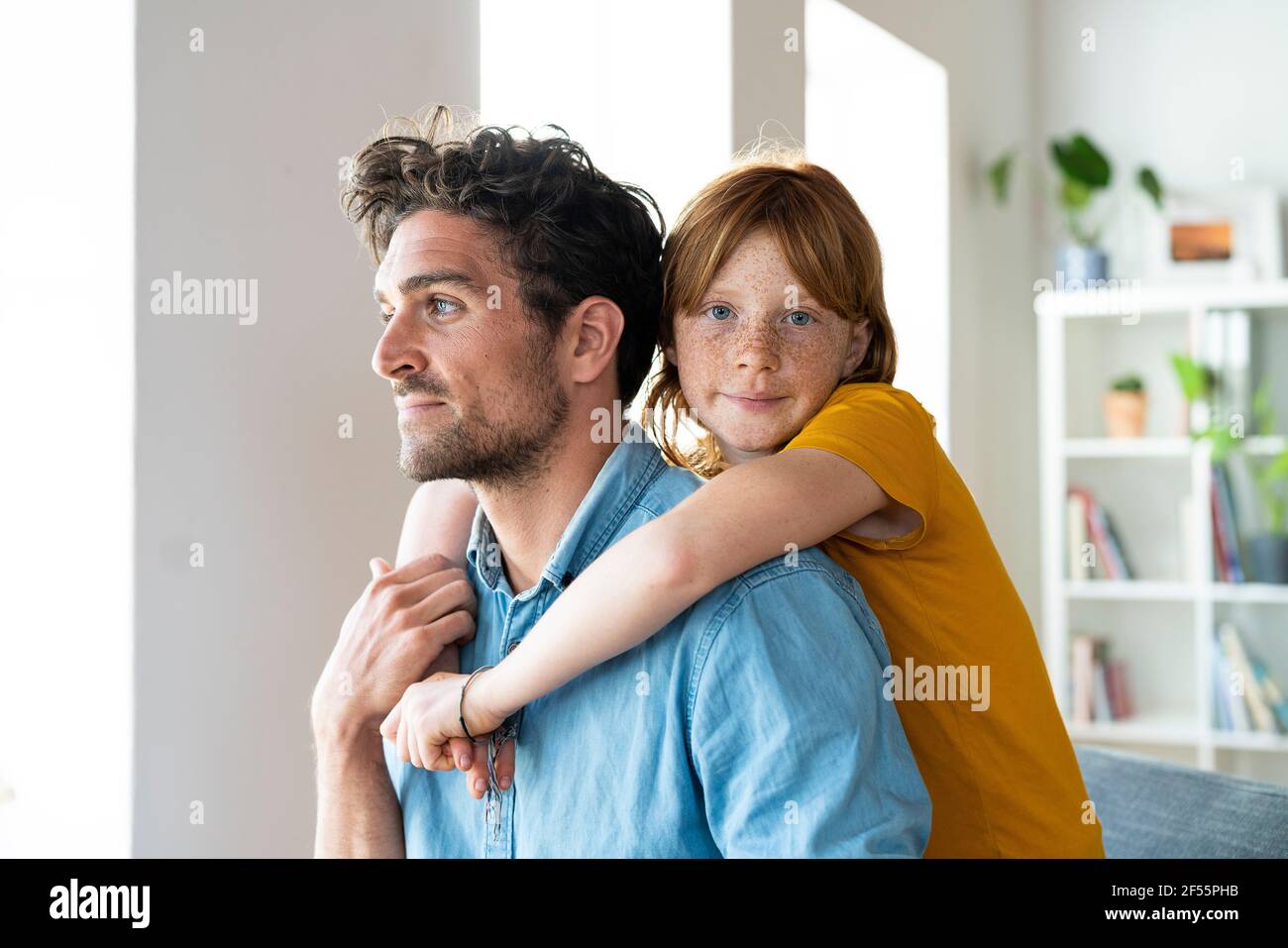 Figlia con gli occhi blu che abbracciano il padre in soggiorno Foto Stock