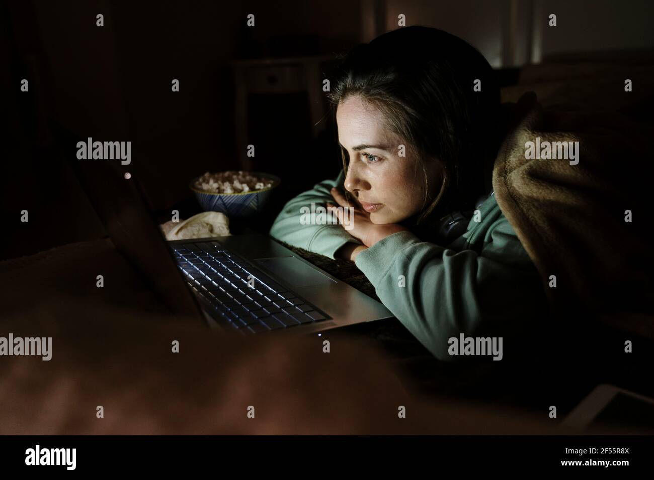 Donna con popcorn guardare film su computer portatile al buio mentre rilassarsi a casa Foto Stock
