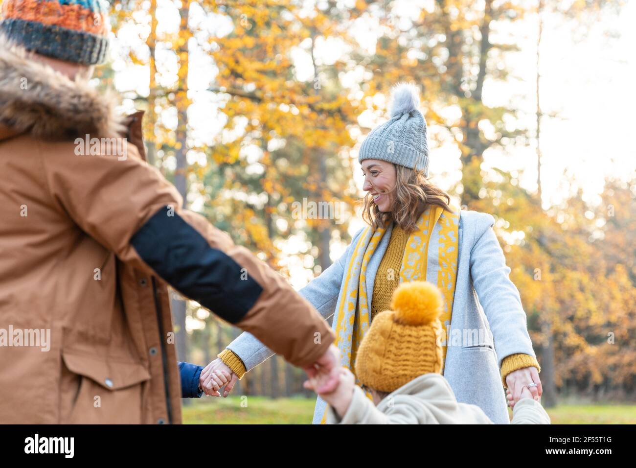 Madre sorridente che tiene le mani dei bambini mentre si gioca insieme nella foresta Foto Stock
