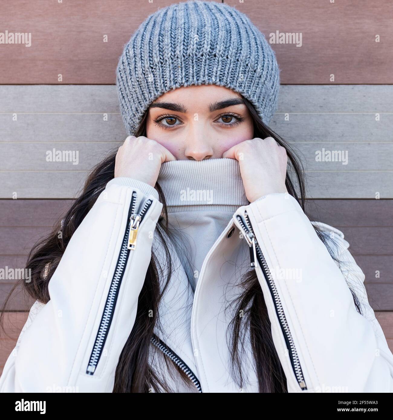 Bella ragazza teenage in cappello a maglia che copre la sua bocca con maglione contro il muro Foto Stock
