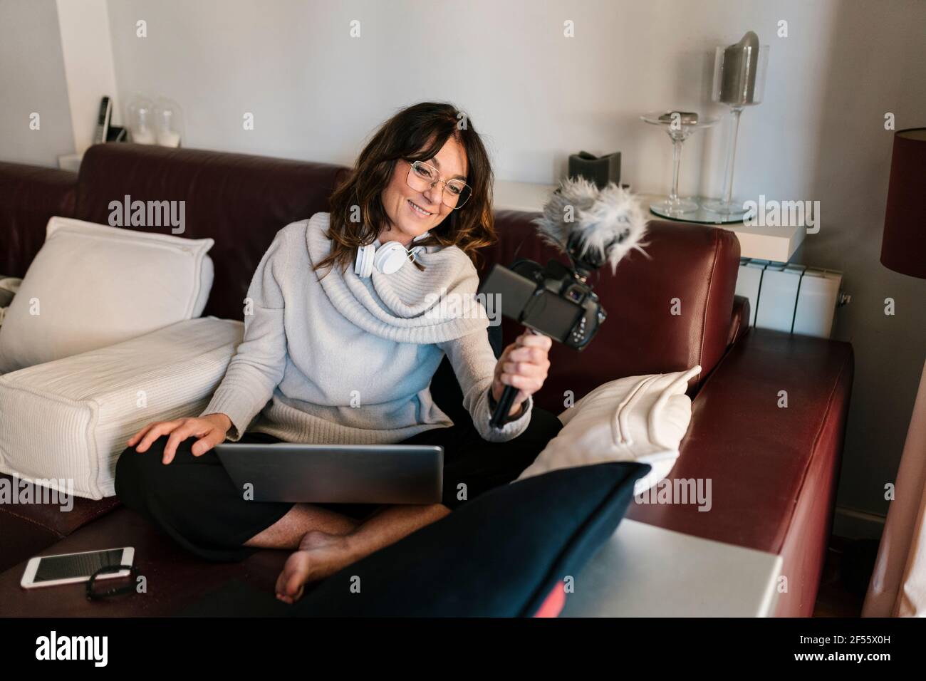 Sorridente vlogger femmina con computer portatile utilizzando la fotocamera mentre vlogging a. casa Foto Stock