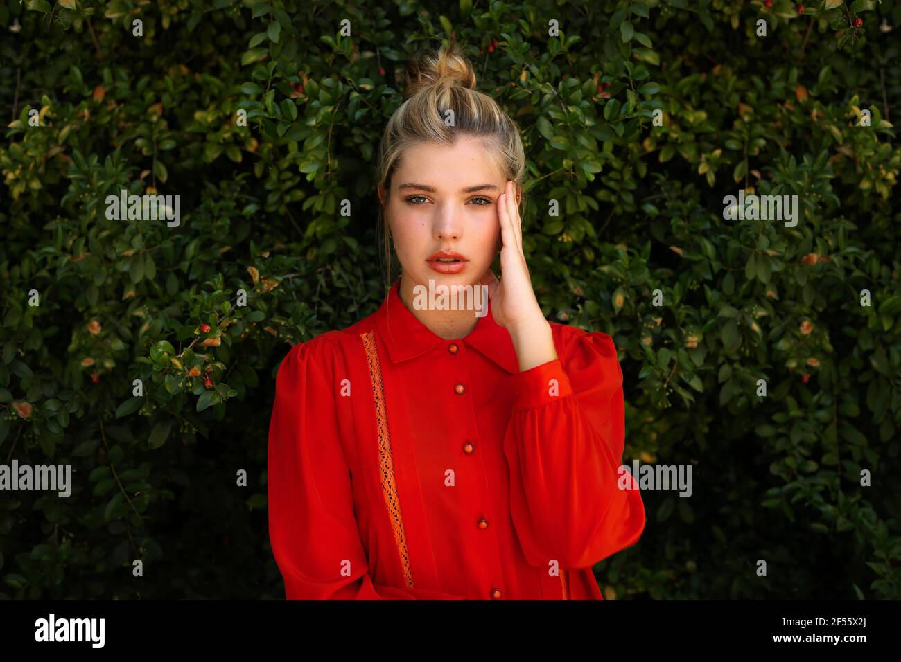 Bella donna in camicia rossa con testa in piedi a mano contro piante Foto Stock