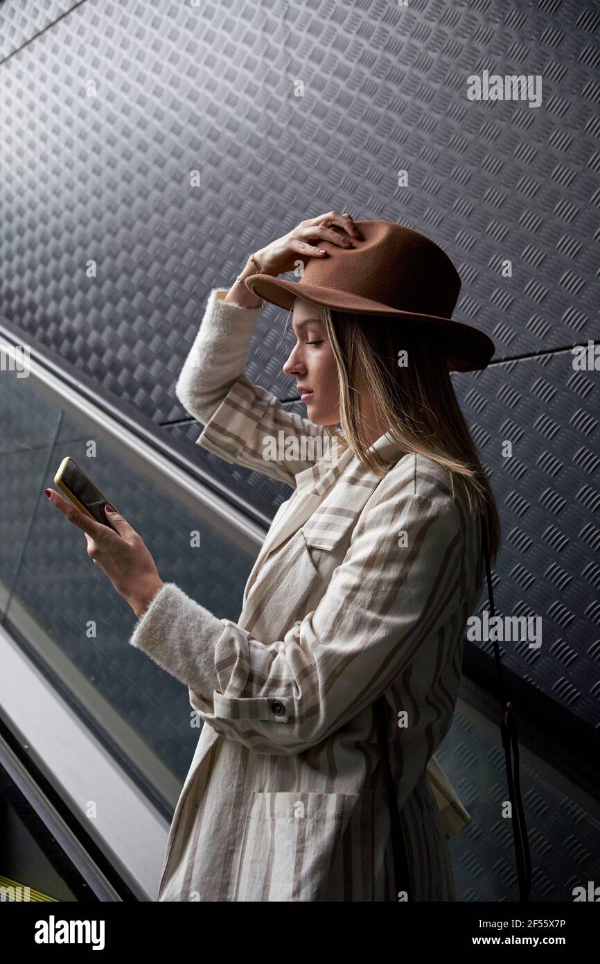 Donna che guarda il telefono cellulare mentre si è in piedi sulla scala mobile Foto Stock