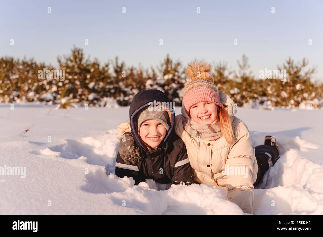 Simpatici fratelli che giacciono sulla neve contro il cielo durante il tramonto Foto Stock