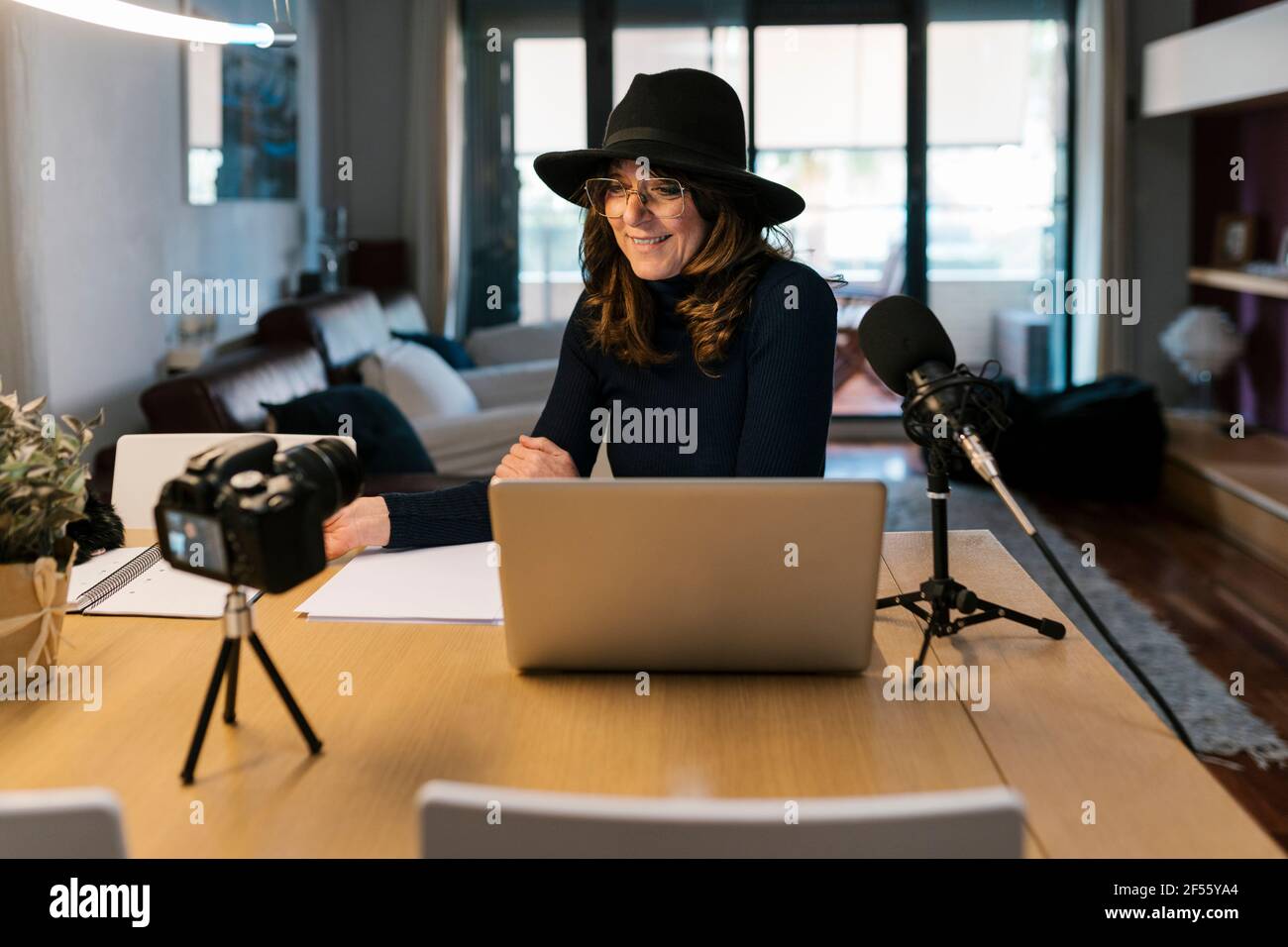 Influencer maturo con notebook e microfono che sorridono durante le riprese sulla fotocamera a casa Foto Stock