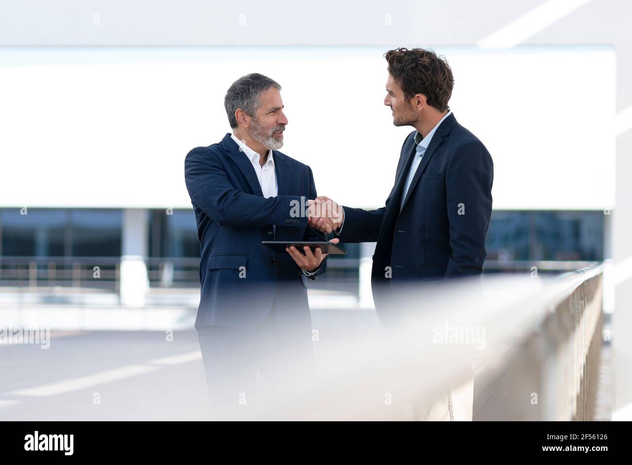 Imprenditore maturo che tiene un tablet digitale mentre fa stretta di mano con un collega in piedi sulla terrazza dell'edificio dell'ufficio Foto Stock