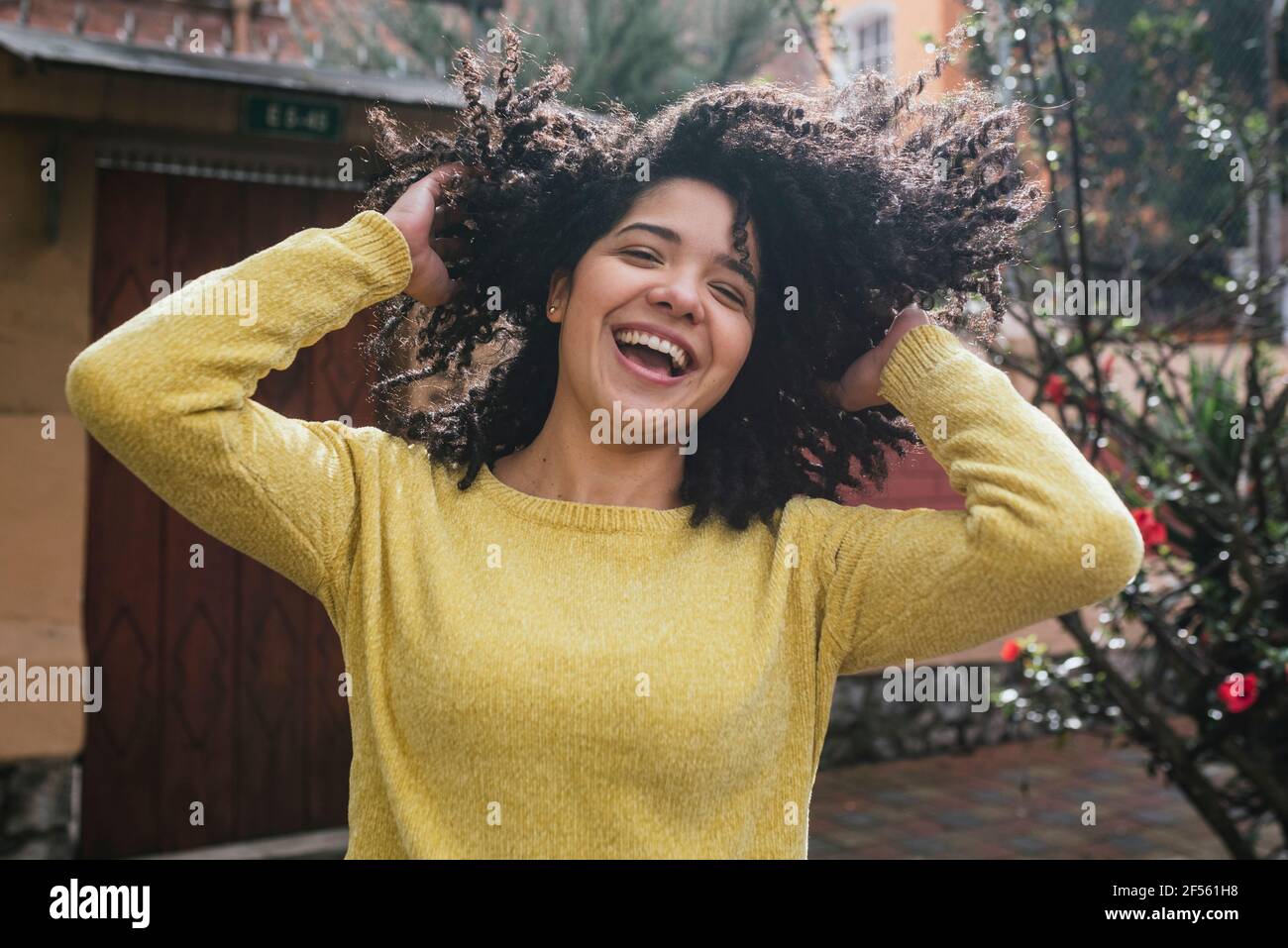 Donna allegra che gioca con capelli neri ricci nel cortile posteriore Foto Stock