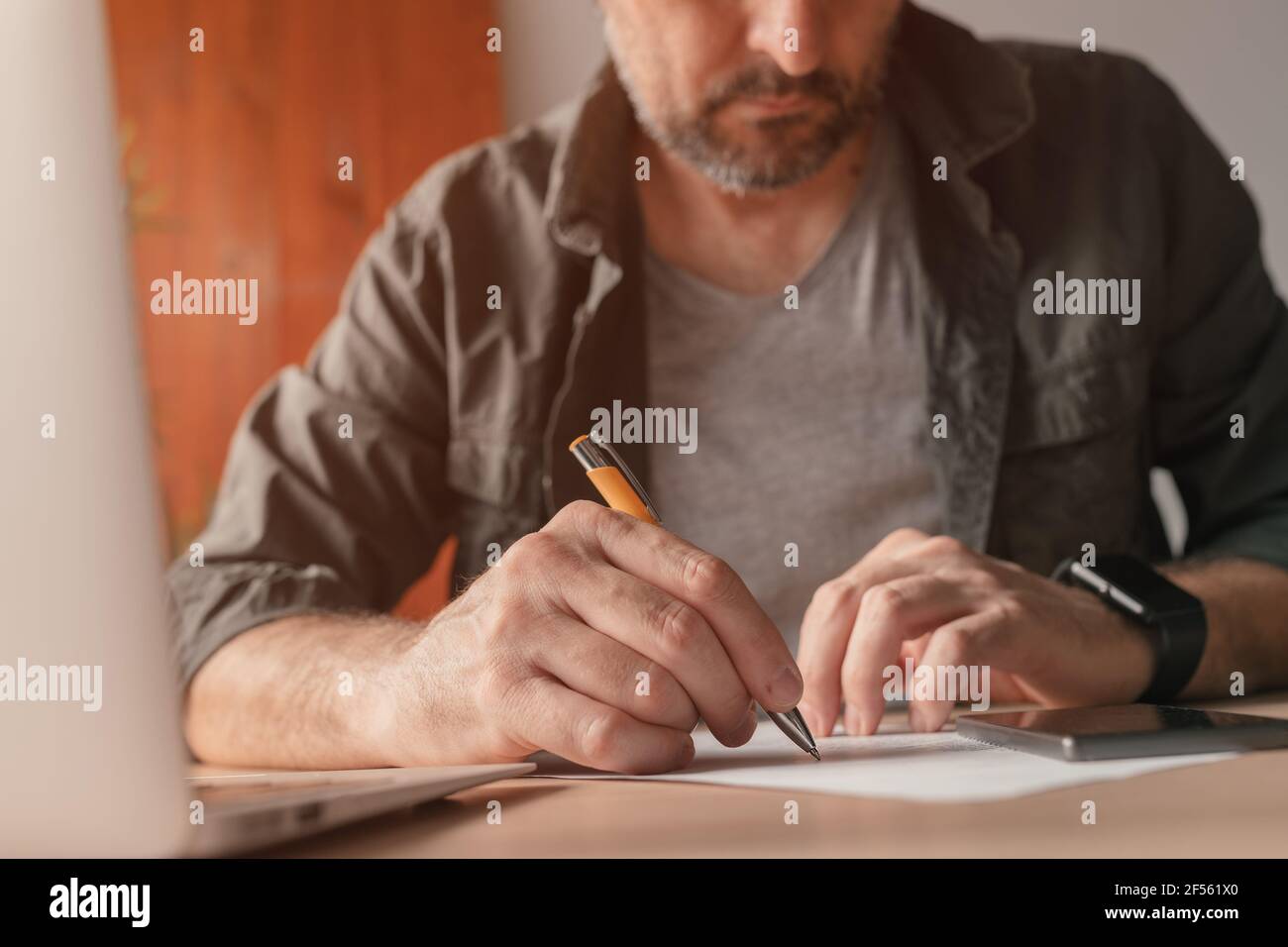 Freelance che scrive note su carta alla scrivania dell'ufficio domestico, primo piano con la messa a fuoco selettiva Foto Stock