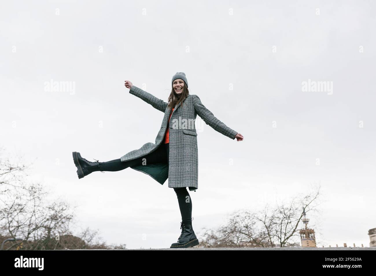 Donna spensierata in piedi su una gamba con le braccia tese contro cielo Foto Stock