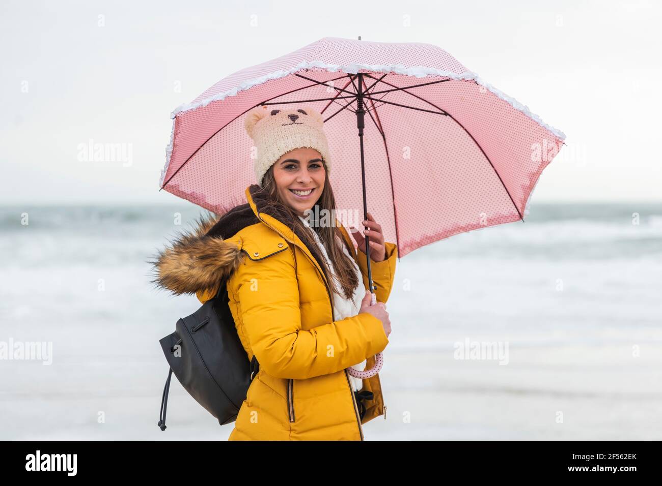 Ritratto di giovane donna in piedi in spiaggia con ombrello in mani Foto Stock