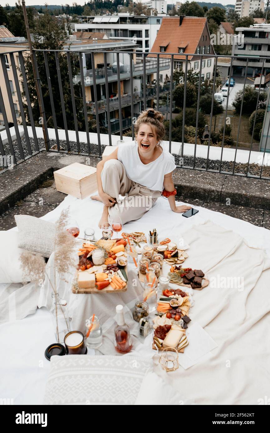 Donna allegra che ride seduto da mangiare e bere su coperta sulla terrazza panoramica Foto Stock
