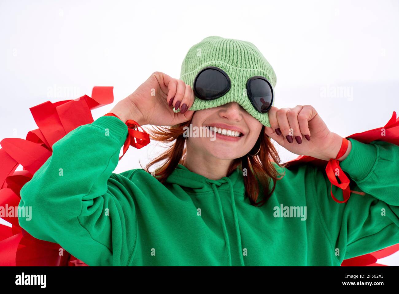 Donna sorridente che tira il cappello a maglia verde contro il cielo Foto Stock