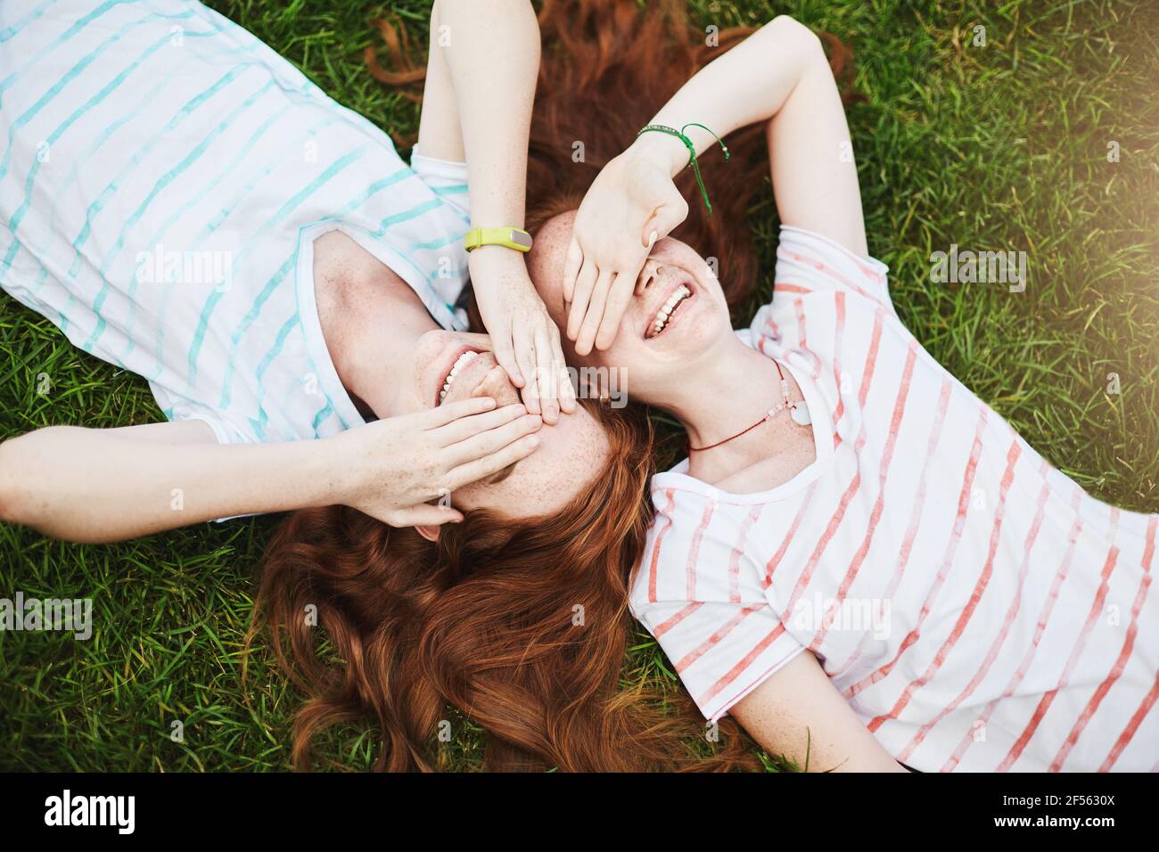 Le sorelle gemelle chiudono gli occhi dal sole, che si stendono a terra in una giornata estiva. Fooling intorno con un amico migliore è così tanto divertimento. Non c'è bisogno di andare a scuola Foto Stock