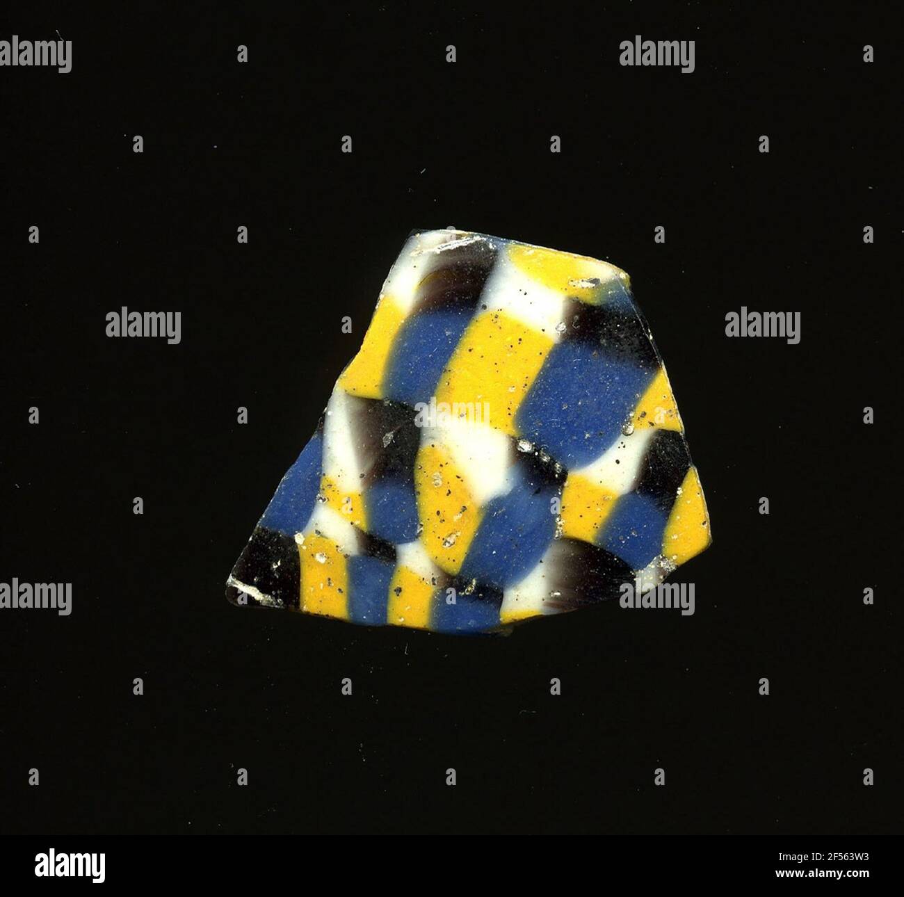 Frammento di vetro a mosaico. Il piccolo frammento di vetro è costituito da quadrati bianchi, neri, gialli e blu, disposti a scacchiera. I singoli quadrati sono talvolta leggermente distorti. In epoca romana furono utilizzati vetri colorati ornati per vasi, mosaici, decorazioni murali e ornamenti di mobili. Per la produzione, diversi vetri colorati sono stati stampati in tubi e aste. Questi sono stati compressi e riscaldati, causando una barra lunga. Il ​​now di vetro affettato aveva un'ampia varietà di motivi amorfi o floreali. Foto Stock