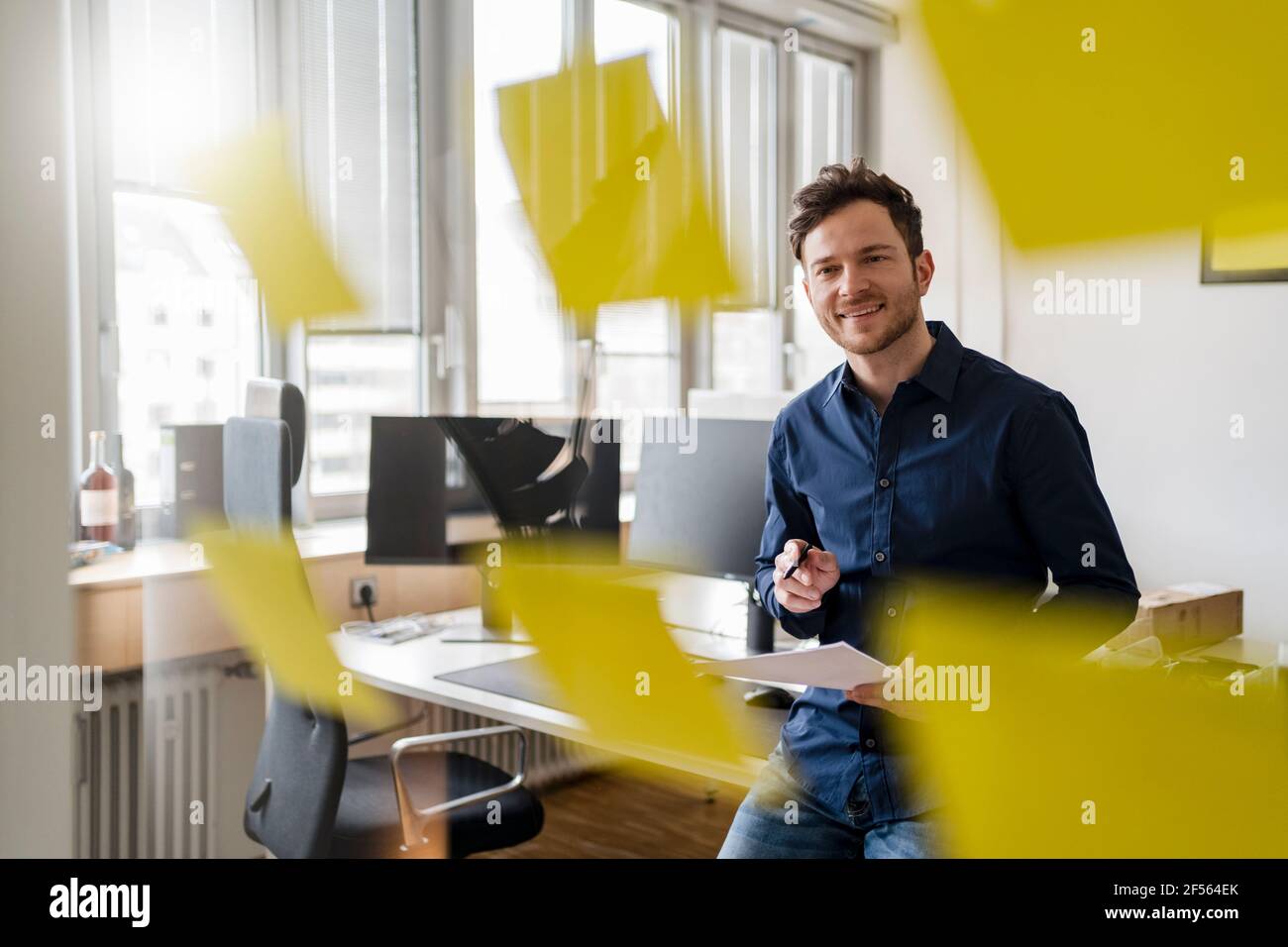 Uomo d'affari sorridente con documento che guarda le note adesive in ufficio Foto Stock