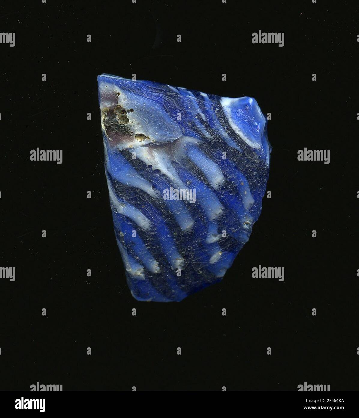 Frammento di un vaso. Una bassa curvatura del frammento di vetro consente l'assegnazione ad un vaso. Il vetro blu è punteggiato da diversi punti bianchi che sono deformati. Per la produzione, diversi vetri colorati sono stati sagomati a tubi e aste. Questi sono stati compressi e riscaldati, causando una barra lunga. Il vetro affettato ​​now aveva differenti motivi amorfi o floreali. Successivamente, molte di queste piastrine sono state piegate, riscaldate di nuovo e pressate in una forma vascolare. Burry per l'elaborato processo di fabbricazione e la sua fragilità è stato uno degli articoli di lusso dell'antichità. Foto Stock