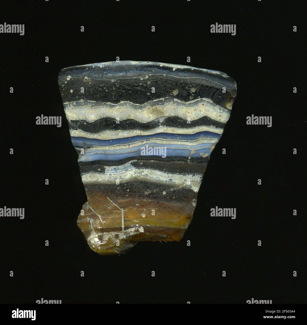 Frammento di un vaso. Una curvatura bassa e il bordo risultante del frammento di vetro consentono l'assegnazione ad un vaso, eventualmente uno shell. Il vetro da scuro a marrone chiaro è attraversato da strisce orizzontali bianche e blu. All'interno ci sono tre strisce bianche. Per la produzione, diversi vetri colorati sono stati stampati in tubi e aste. Questi sono stati compressi e riscaldati. Burry per l'elaborato processo di fabbricazione e la sua fragilità includeva il vetro degli articoli di lusso dell'antichità. Foto Stock